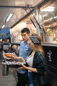 A young couple savoring delicious street food at a bustling food truck in the evening.