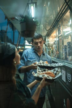 A couple shares delicious fast food at a bustling night food truck.