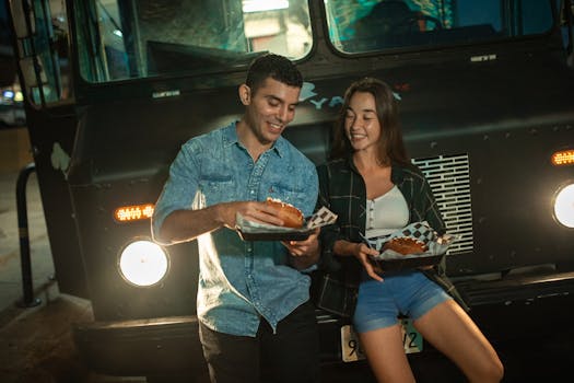Smiling couple eating from a food truck at night, sharing a joyful moment.