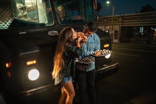A young couple enjoying food from a truck at night, highlighting urban dining.