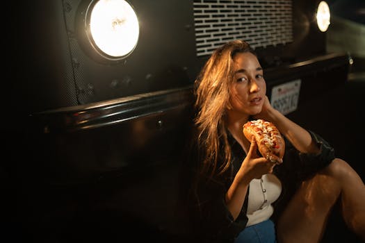 Young woman savoring a tasty hot dog next to a food truck at night.