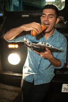 A young man savoring a delicious snack from a food truck at night, embodying urban life.
