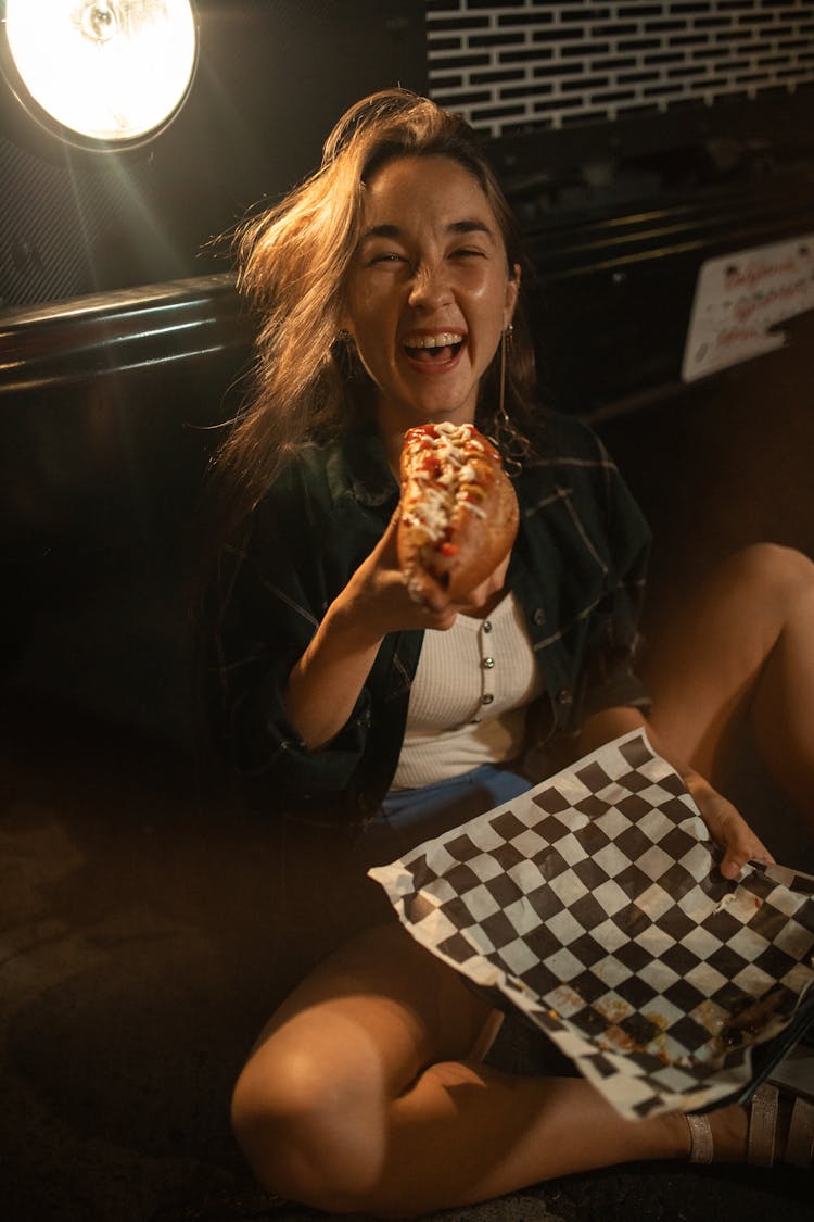 A Woman Smiling While Holding A Hotdog Sandwich