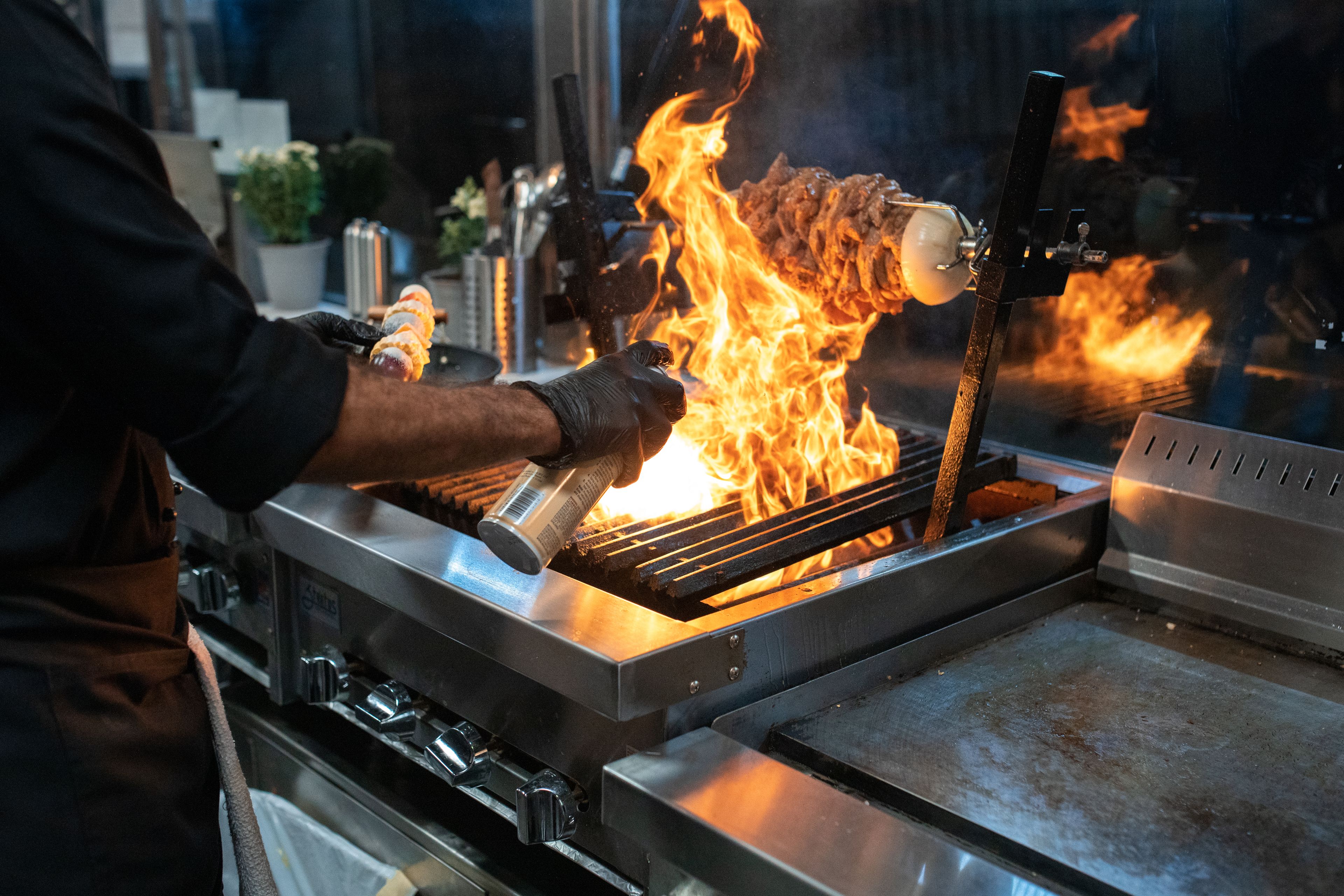 Chef saisissant une pièce de viande au grill, flammes et fumées grasses aspirées par la hotte au-dessus du piano