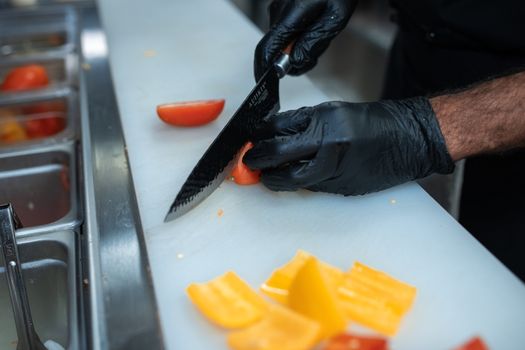 Chef wearing gloves slices peppers in a busy kitchen for meal preparation.