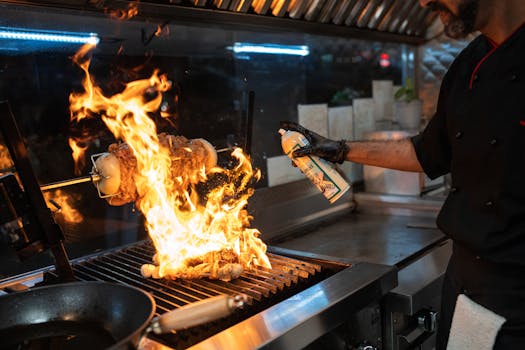 Chef uses a culinary torch to ignite a flaming grill indoors, showcasing dynamic cooking.