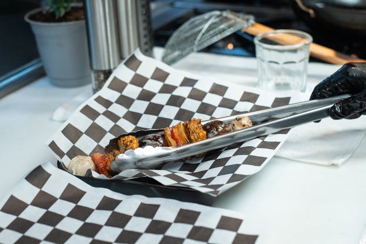 Person Putting Kebab On A Plate Using A Tongs