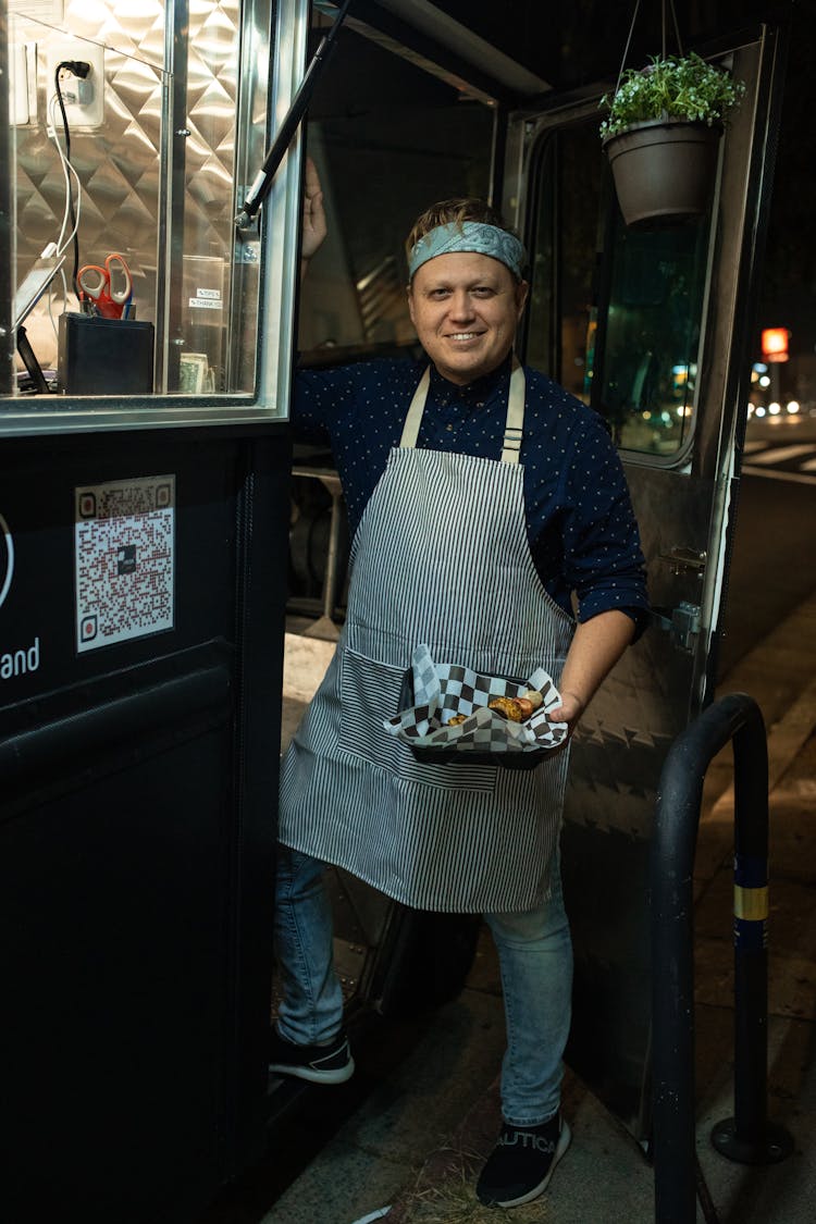 A Man Holding A Food Standing Near A Food Truck