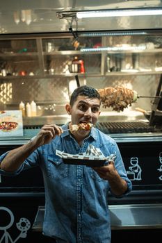 Man savoring a delicious skewer in front of a food truck at a night market.
