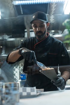 Chef in a food truck kitchen preparing a dish with tongs in hand.