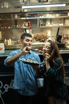 A couple savoring kebabs at a street food truck under night lights.