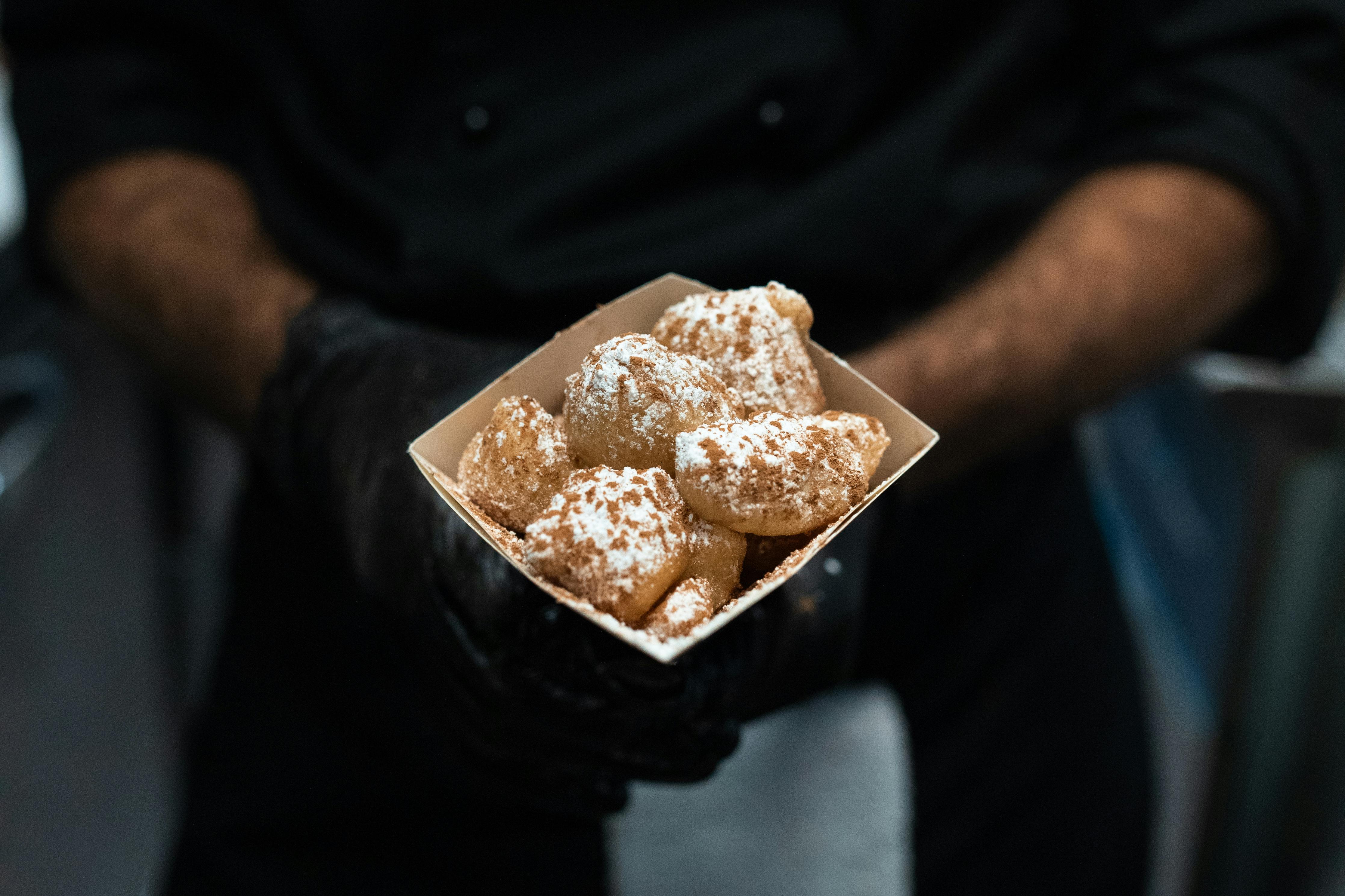 person holding brown and white pastry in a square box