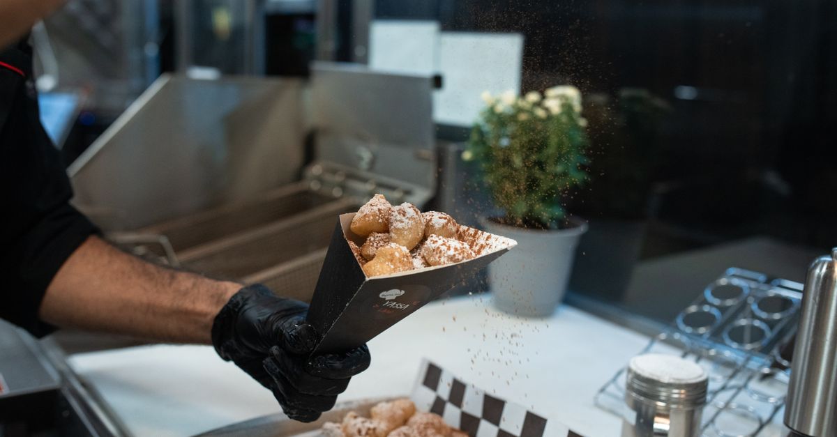 Close-up of freshly prepared beignets in a street food setting, sprinkled with powdered sugar.