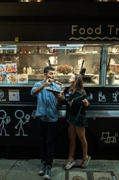 A joyful couple enjoying food at a trendy food truck in the evening.