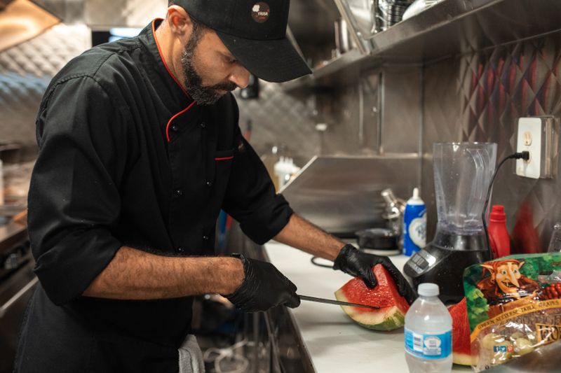 A chef slicing fresh watermelon in a commercial kitchen