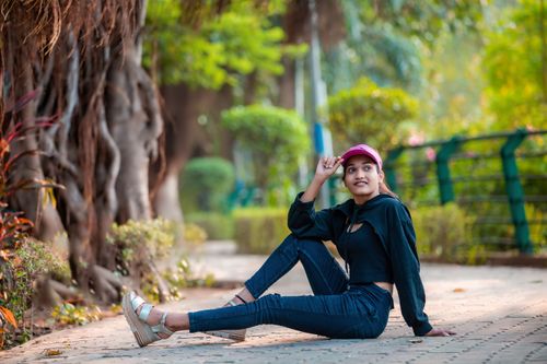 Free Young woman sitting relaxed in a lush park wearing casual attire and a pink cap, enjoying nature. Stock Photo