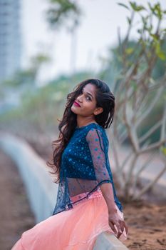 Portrait of a woman with long hair, wearing a stylish outfit, sitting outdoors. 5780526