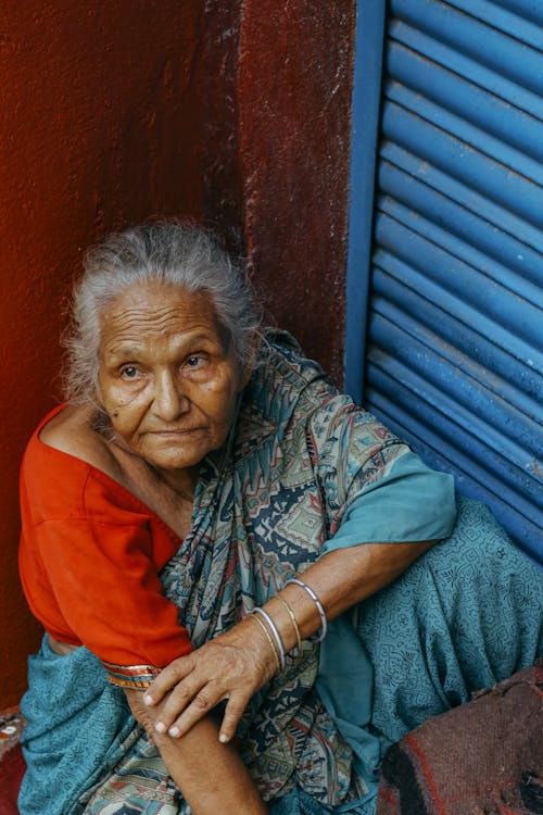 Пожилая этническая женщина, сидящая у стены