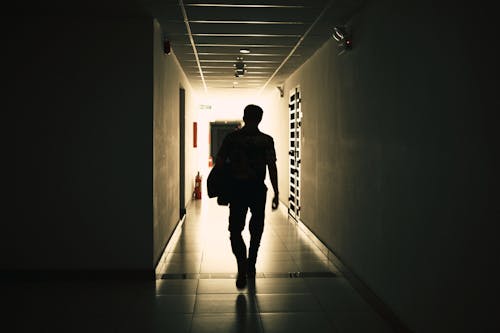 Free Back view silhouette of unrecognizable male walking on narrow empty hall of modern building Stock Photo