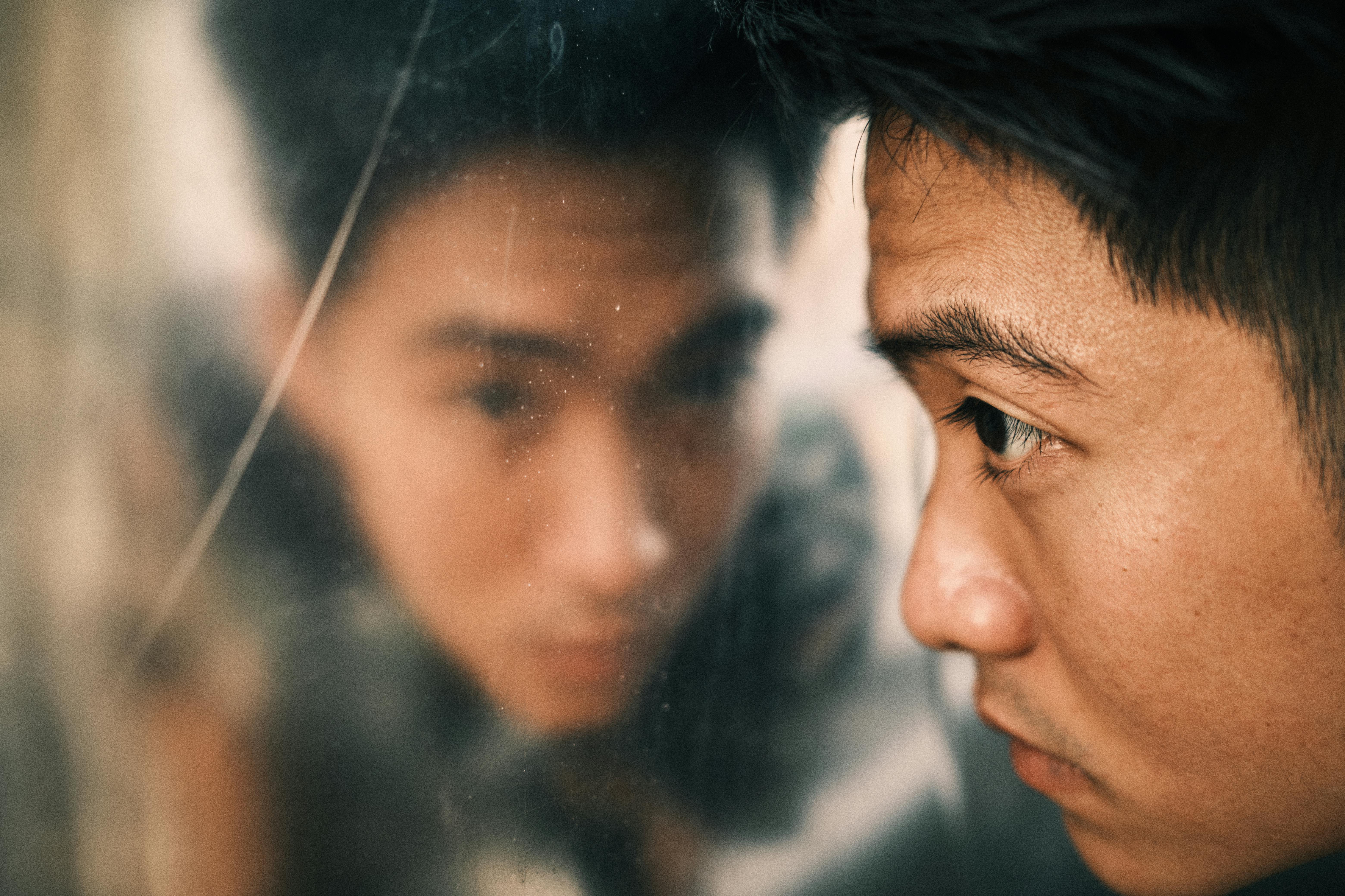 Side view of crop young serious Asian man looking in dirty mirror in daytime