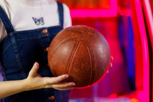 A close-up shot of hands holding a vintage basketball with neon lights in the background.