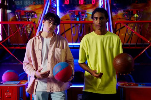 Two young men holding basketballs at an amusement arcade, engaging in a fun indoor game.
