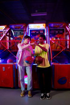 Two teenagers having fun with basketball games at an amusement arcade.