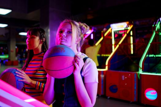 Two young women playing basketball games at a vibrant arcade, enjoying a fun night out.
