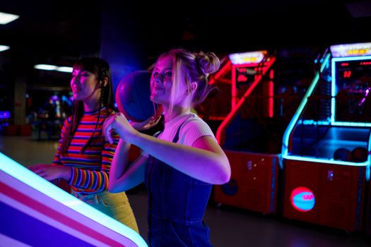 Two young women enjoying arcade games and basketball in a vibrant amusement center.