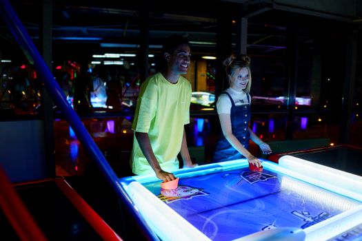 A smiling couple playing air hockey in a neon-lit arcade setting, enjoying leisure time together.