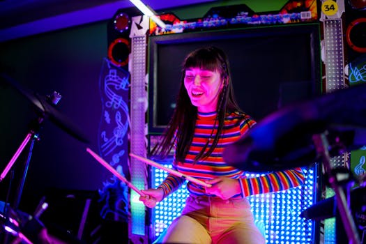 Asian woman playing drums with enthusiasm and joy indoors under vibrant lighting.