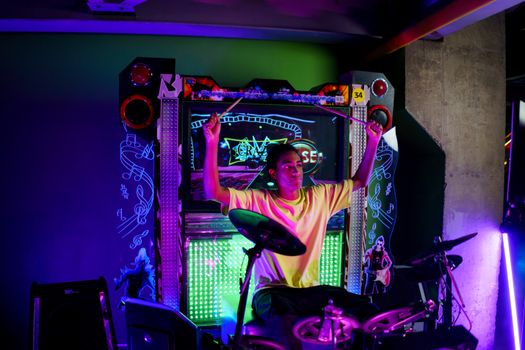 A young musician passionately plays electronic drums at an illuminated arcade setup.