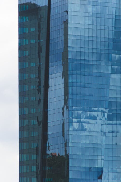Contemporary high rise skyscraper with glass walls reflecting cloudy sky in urban city center