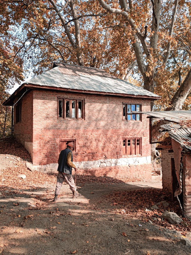 Man Walking With Cane Near A Brick House 