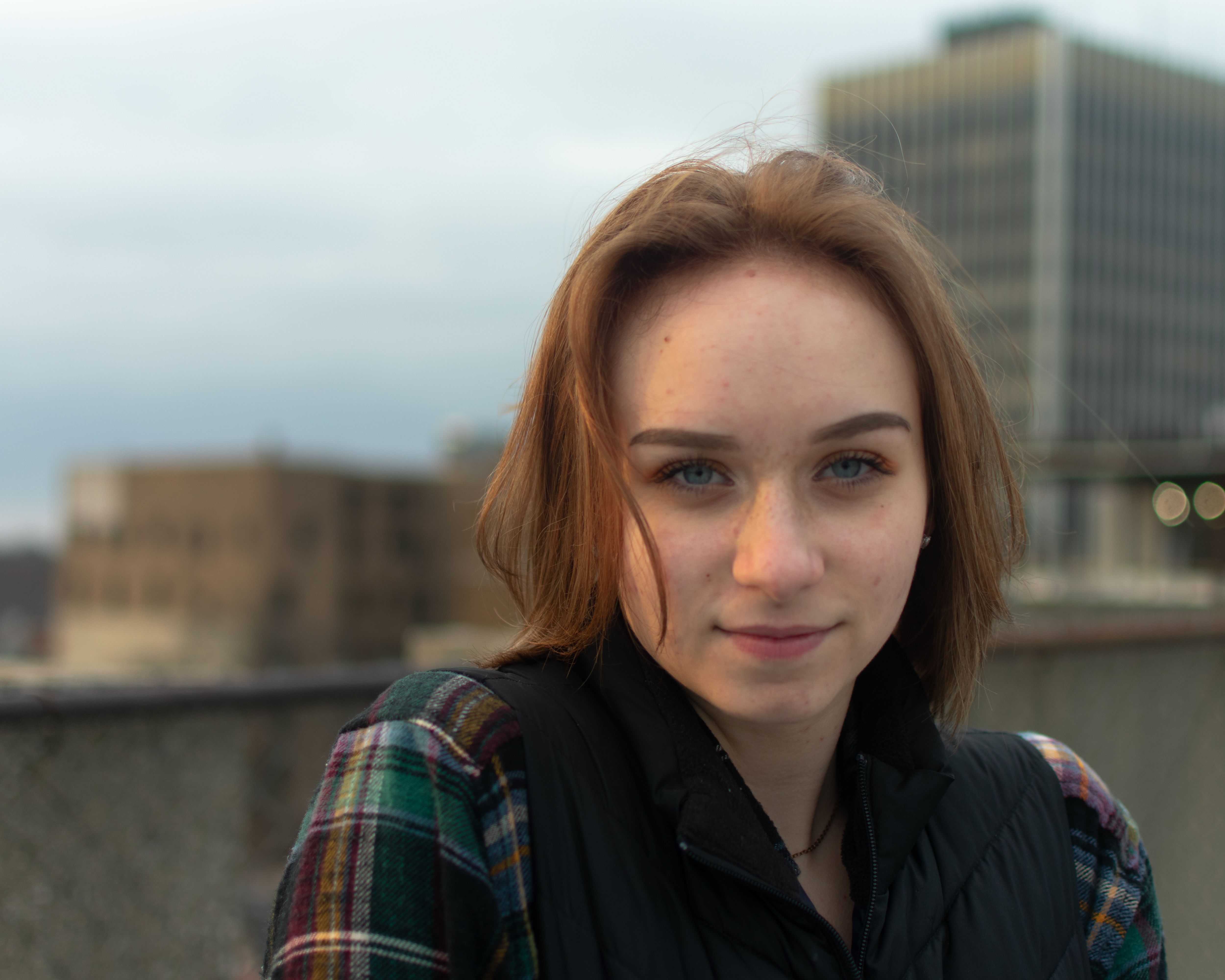 Portrait of a young woman with urban buildings in the background, showcasing natural beauty and daylight.