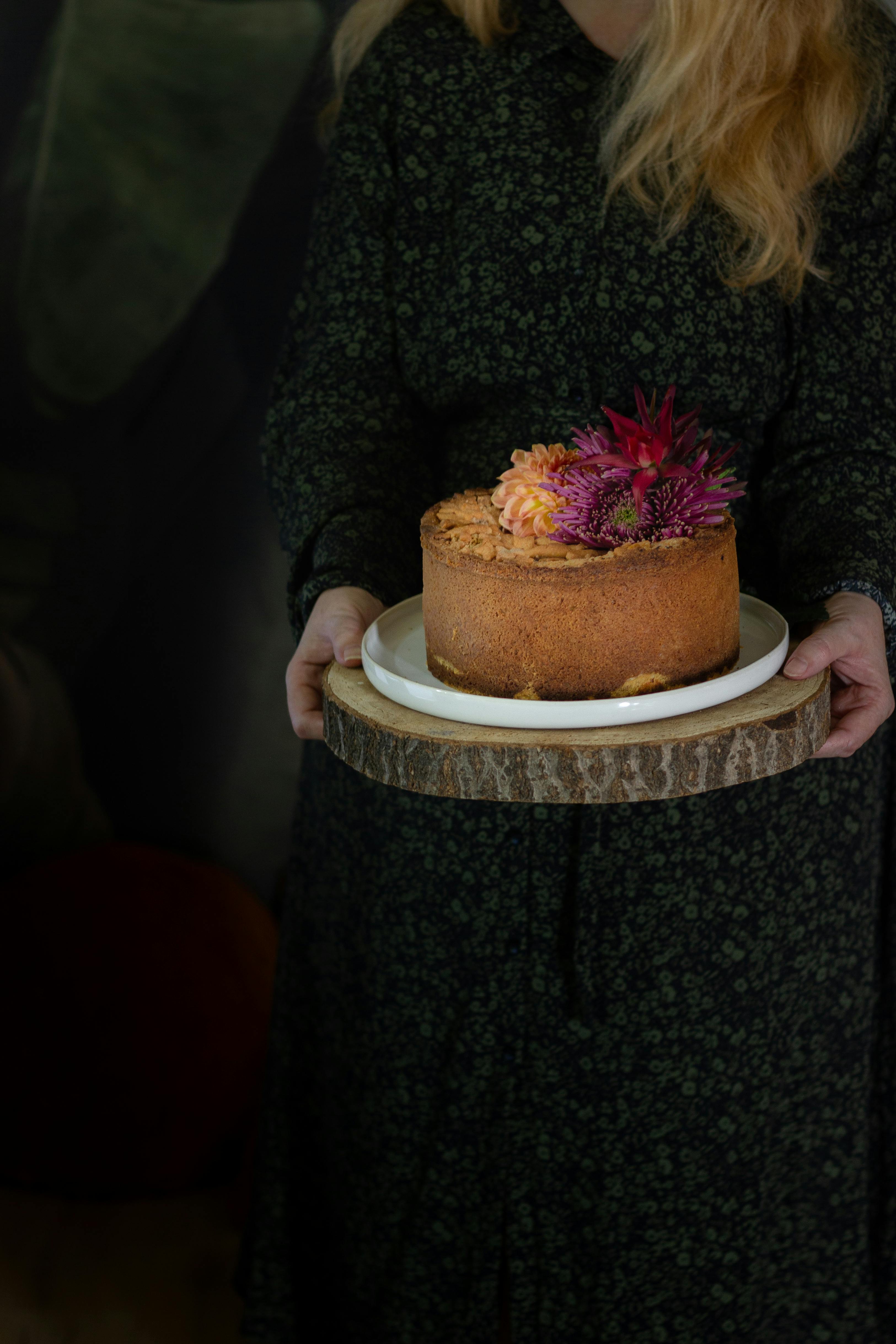 Charming rustic cake decorated with vibrant flowers, held on a natural wooden stand.
