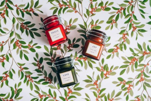 Free Collection of scented candles labeled Peace, Joy, Love on a leafy holiday background. Stock Photo