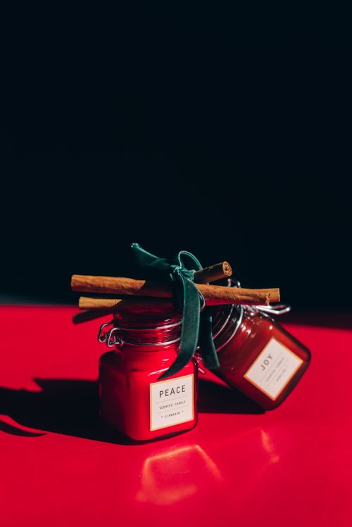 Free Close-up of stylish red candle jars labeled 'Peace' and 'Joy' with cinnamon sticks. Stock Photo