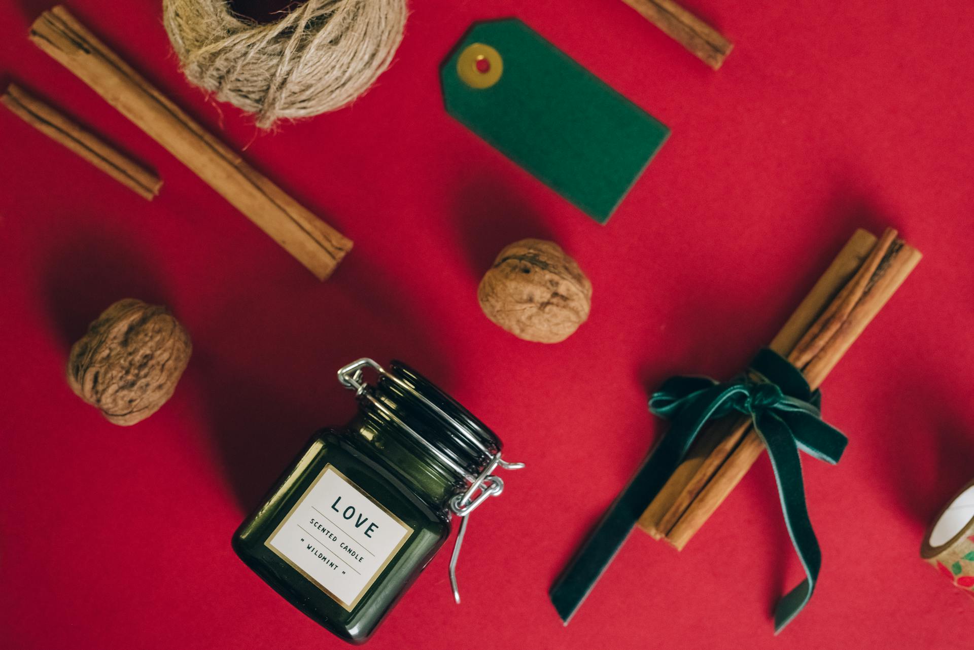 Festive scented candle with cinnamon and walnuts on red backdrop, evoking holiday warmth.