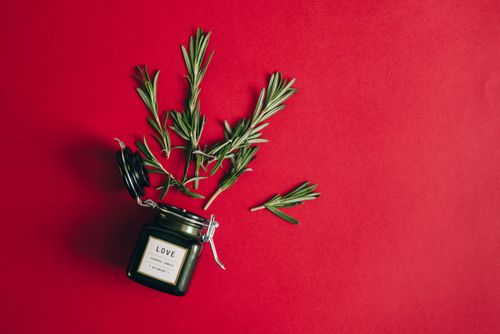 Free A scented candle jar with rosemary sprigs on a vibrant red surface. Stock Photo