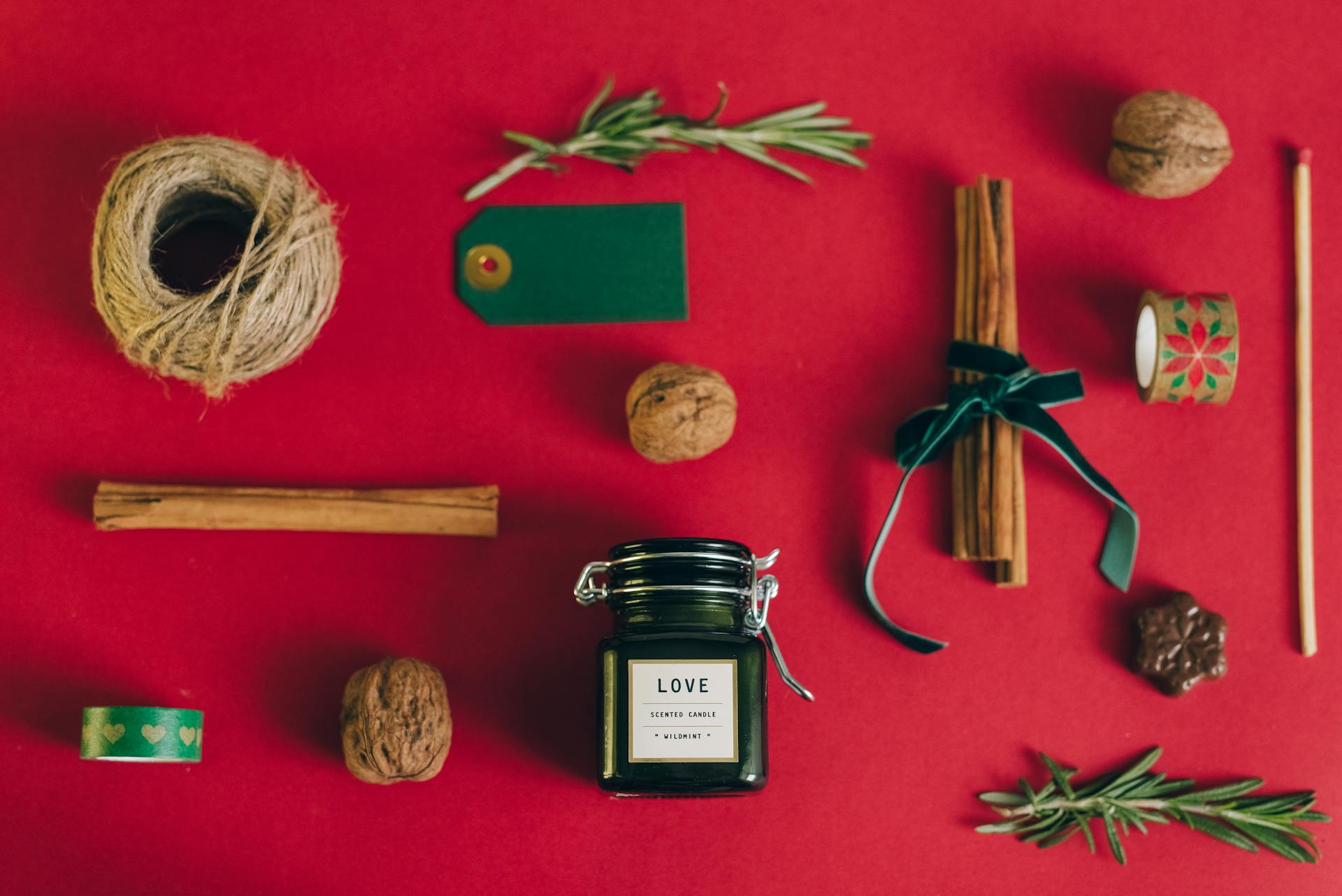 A flat lay of a scented candle with gift wrapping items on a festive red surface.