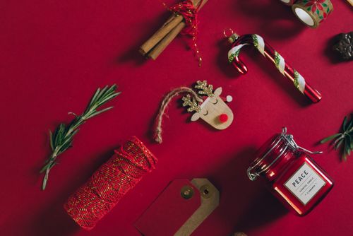 Free Holiday-themed flat lay of Christmas items including a scented candle, gift tags, and candy cane on a red surface. Stock Photo