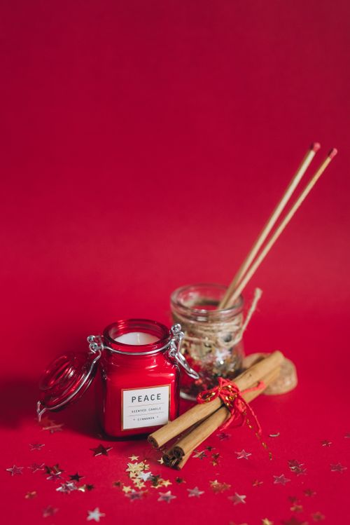 Free A red scented candle and cinnamon sticks on a festive red surface with star confetti. Stock Photo