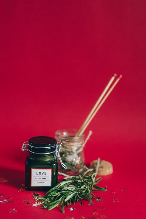Free Scented candle with herbs and decorations on a vibrant red surface, creating a festive atmosphere. Stock Photo