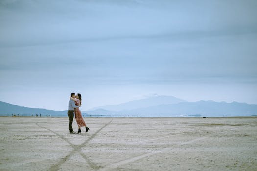 Loving couple embraces in an expansive desert landscape with mountains in the background.