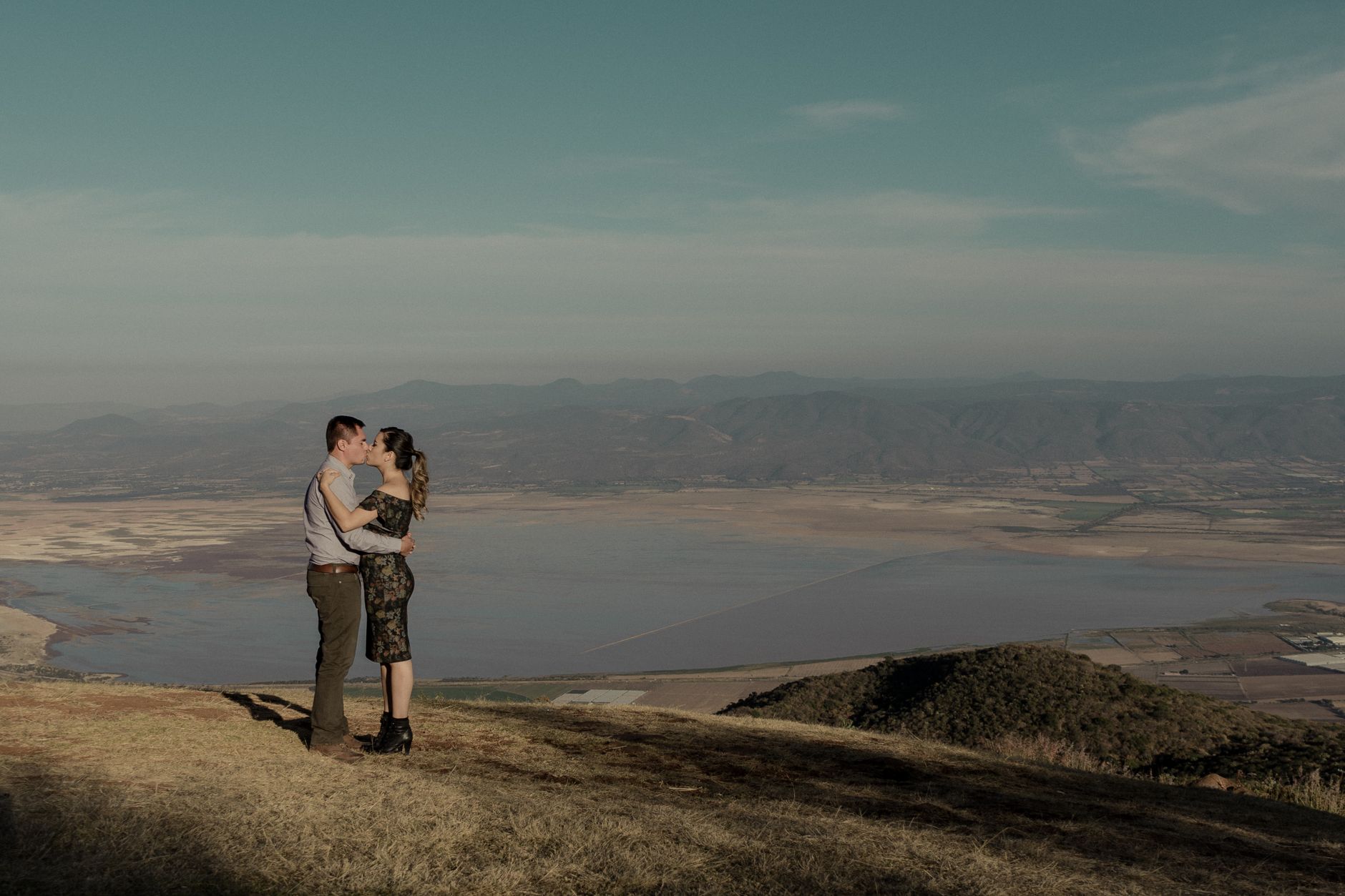 couple embracing at a scenic mountain overlook just after a proposal, champagne glasses visible in the foreground