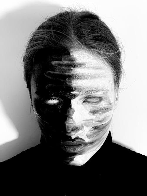 Black and white of scary female with spooky greasepaint on face wearing turtleneck rolling eyes while standing on white background