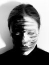 Black and white of spooky weird female wearing pullover with paints on face rolling eyes while standing on white background