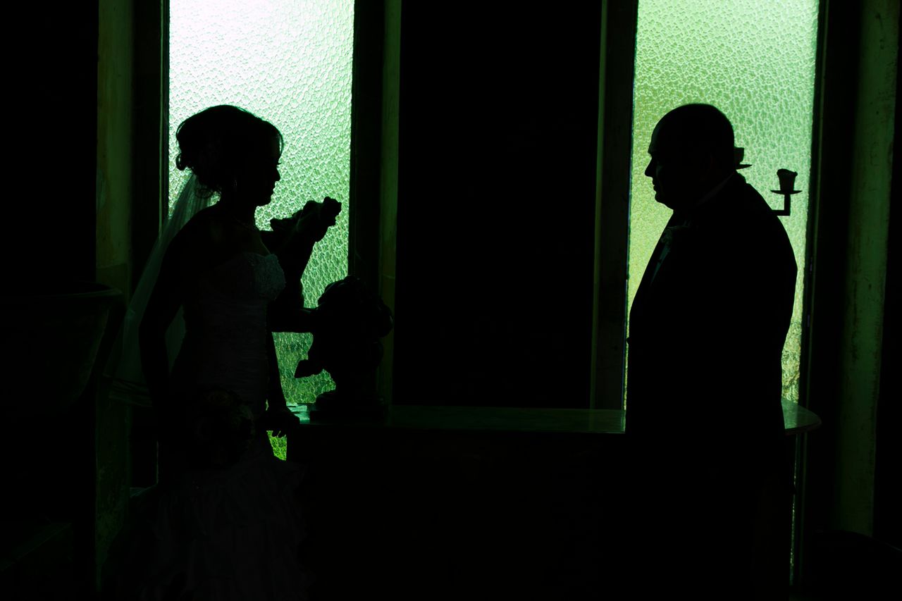 artistic silhouette of a bride and groom facing each other in a dark r