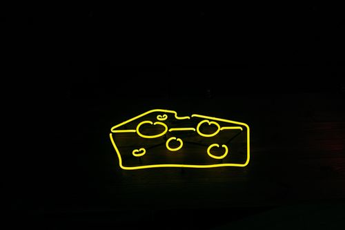 Free A bright yellow neon sign shaped like cheese against a black background, creating a modern and eye-catching design. Stock Photo